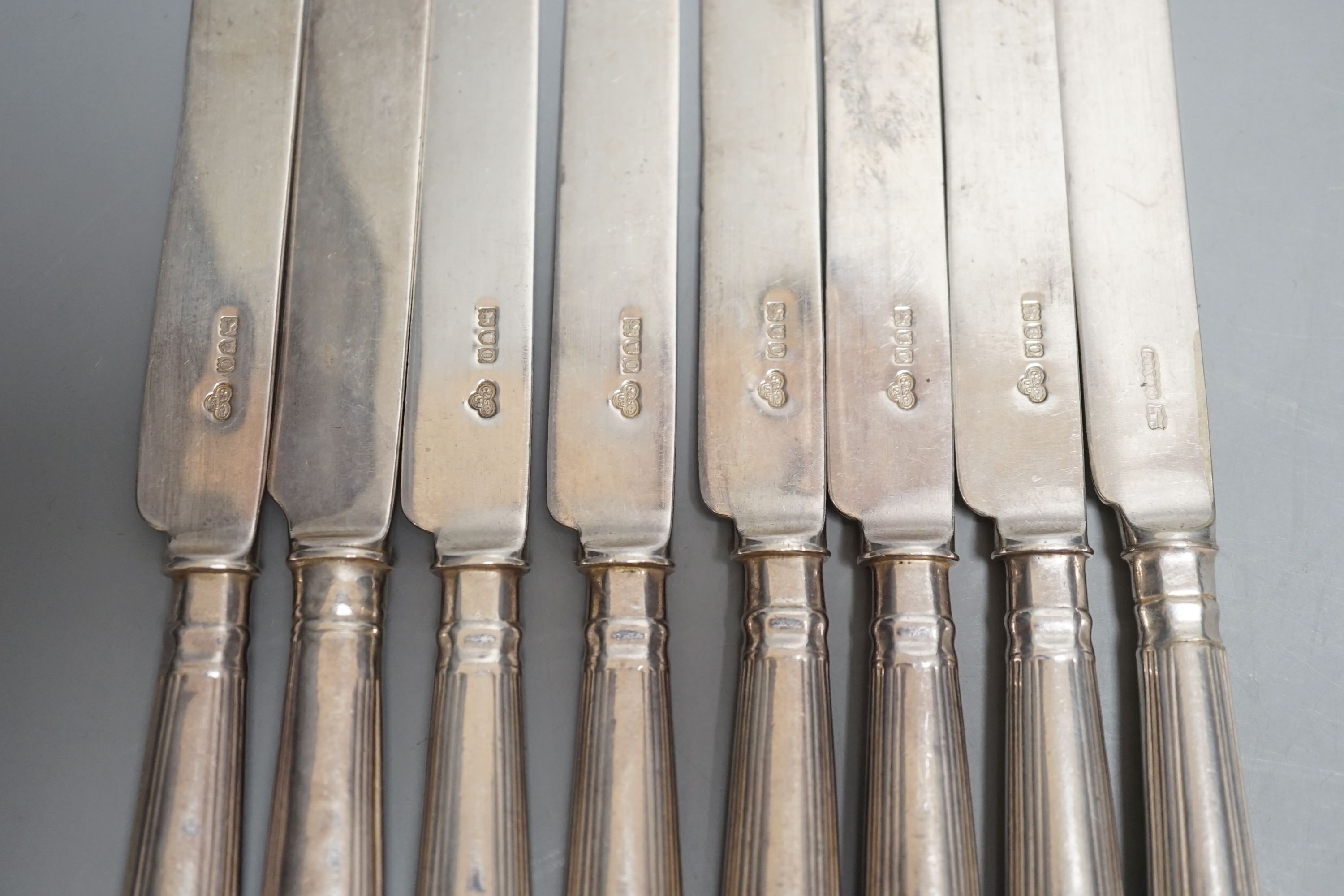 A set of seven Edwardian silver fiddle and shell pattern dessert knives, Goldsmiths & Silversmiths Co Ltd, London, 1909 and a similar plated knife.